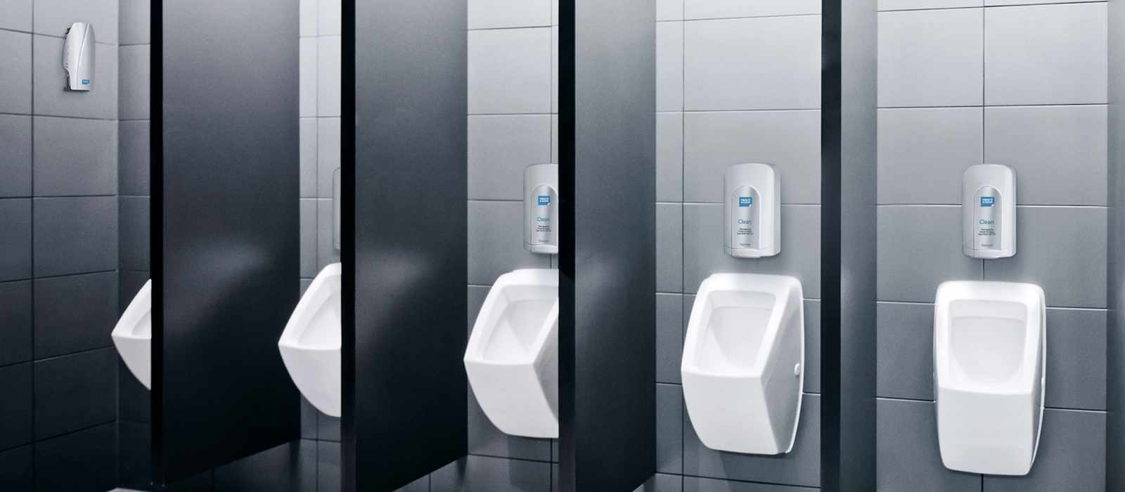 A row of clean, modern urinals in a tiled public restroom, each separated by black partitions. Above each urinal, a wall-mounted soap or sanitiser dispenser is visible, suggesting a focus on hygiene. The restroom has a sleek and minimalistic design.